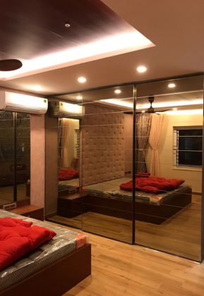 A cozy bedroom with a bed and a mirror on the wall, showcasing mirror wardrobes in its design.